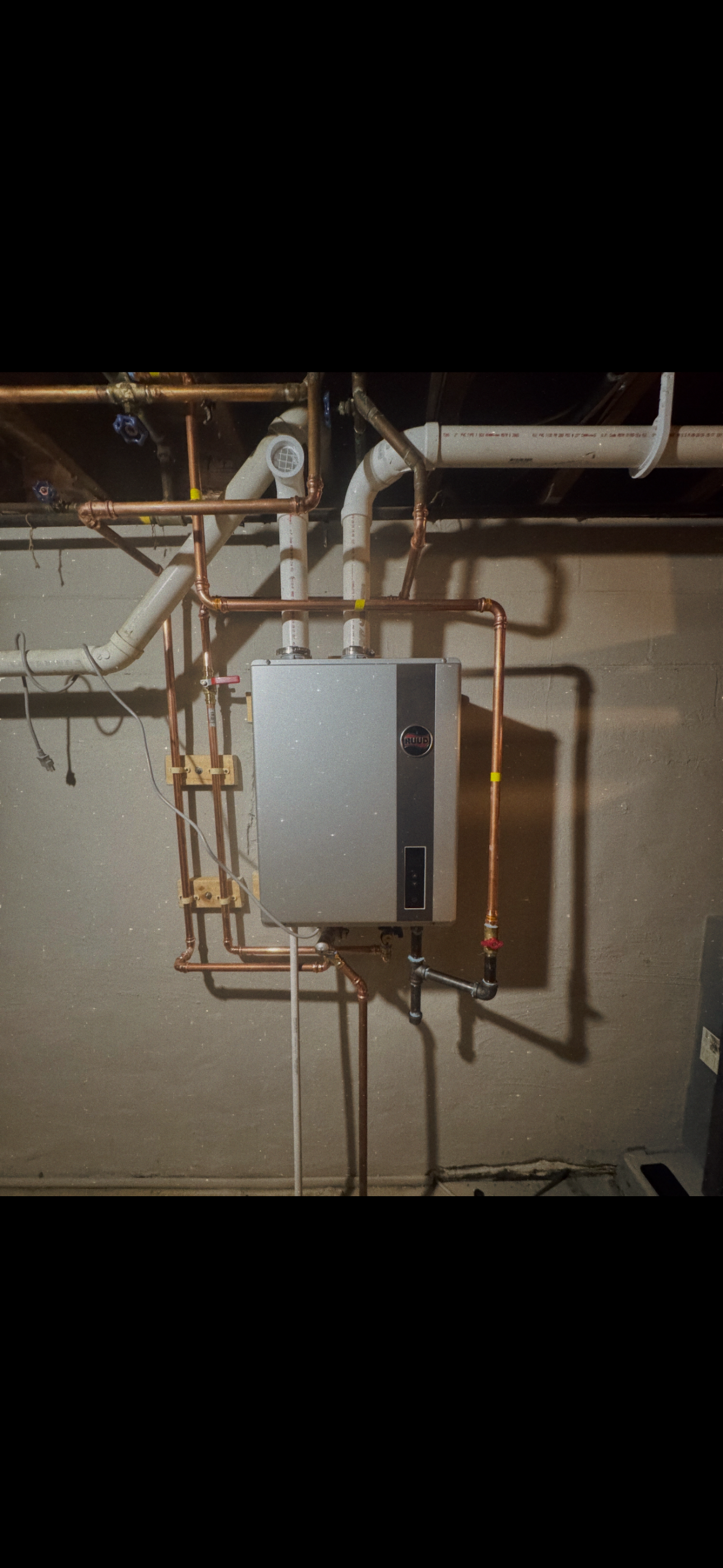 Copper pipes and a boiler are mounted on a concrete wall.