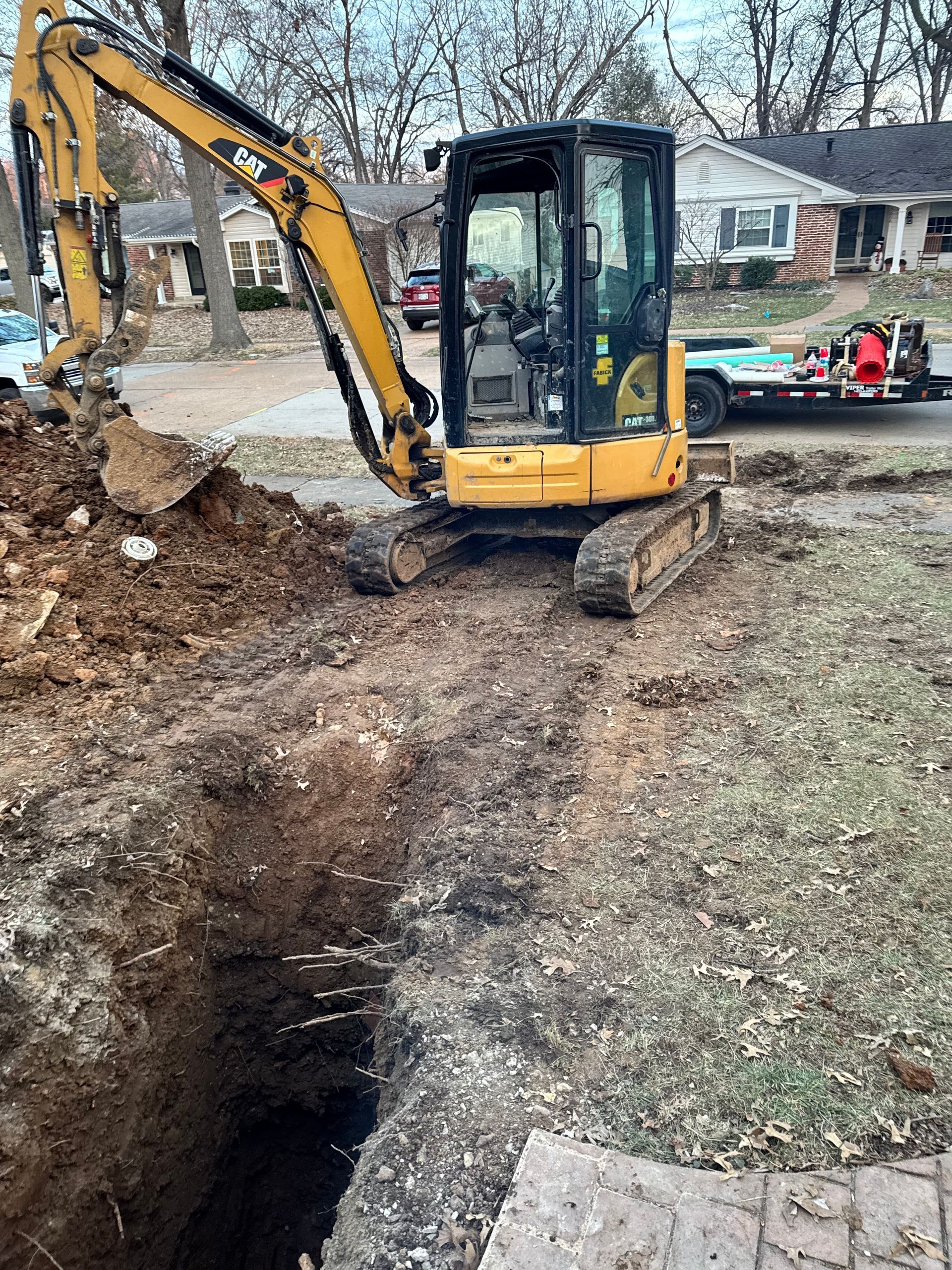 Yellow excavator digging a trench in a yard near a residential street.