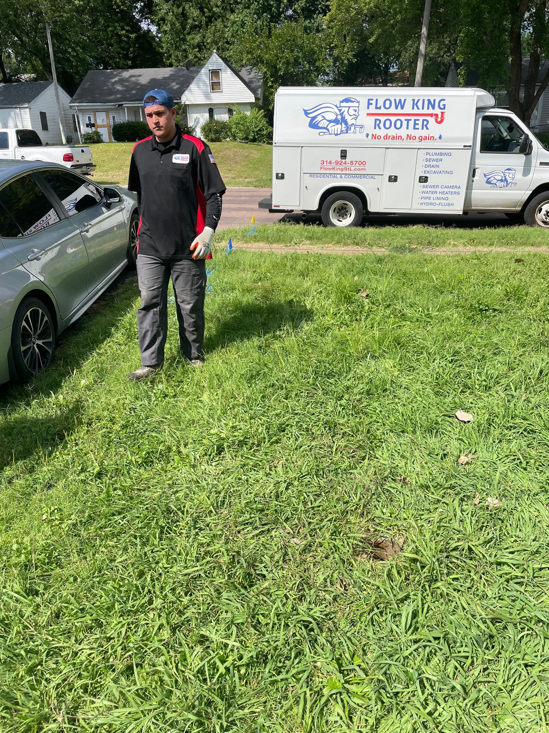 Plumber in uniform walking on grass near white work van with company logo parked on a residential street.