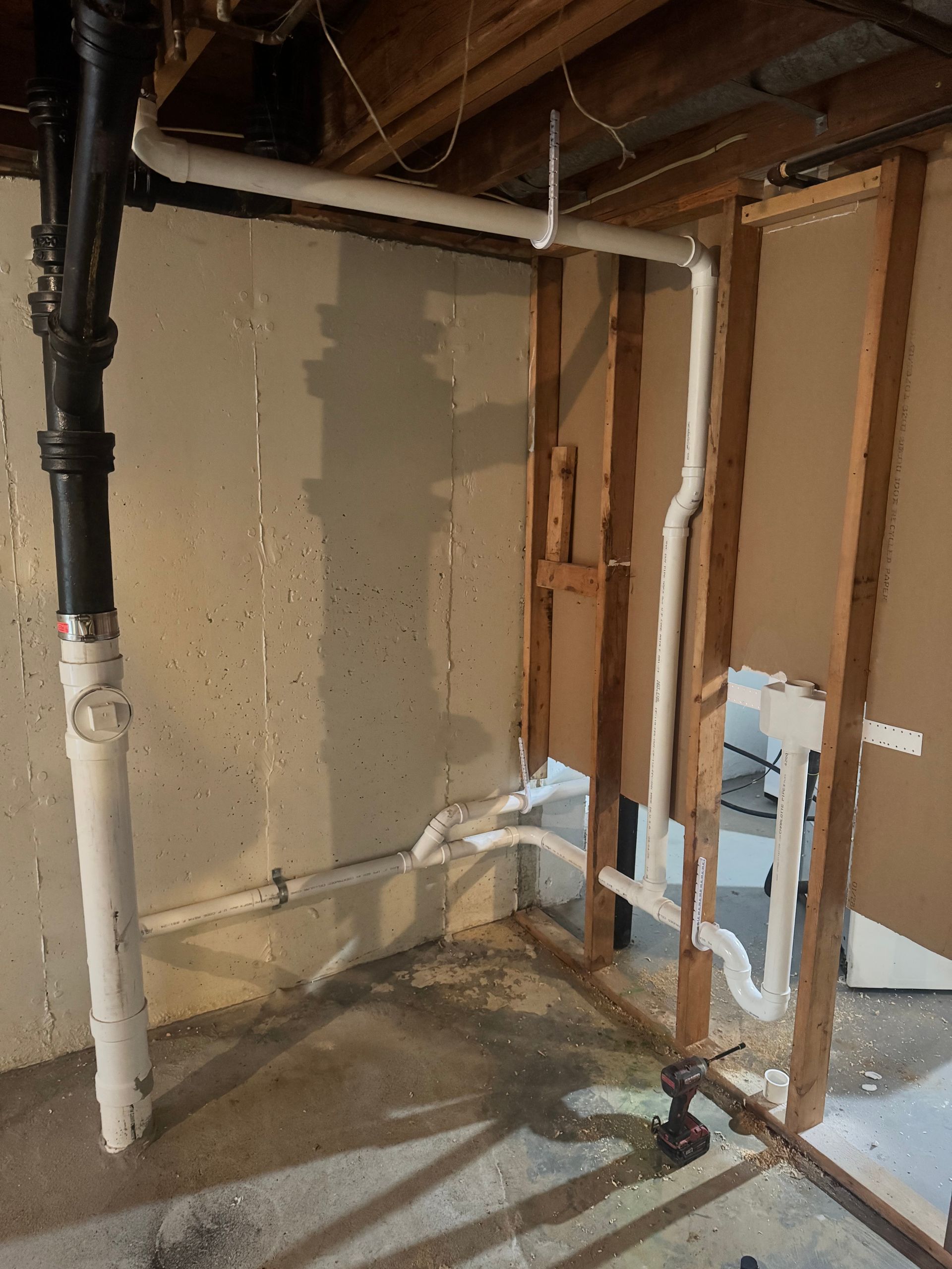 Plumbing pipes installed in a basement, with exposed wooden framing and drywall.