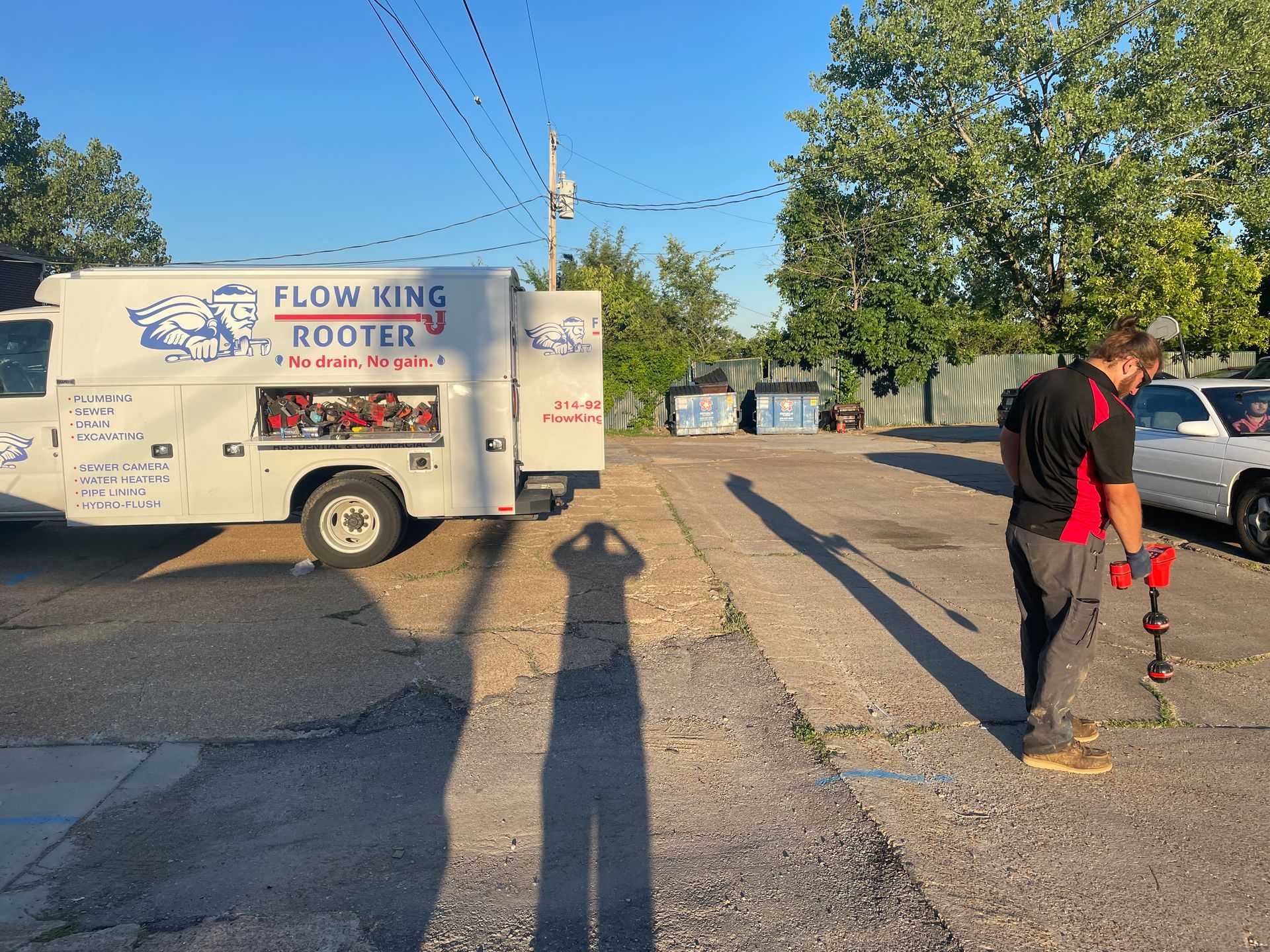 A worker stands with a tool near a plumbing service truck in a parking lot.