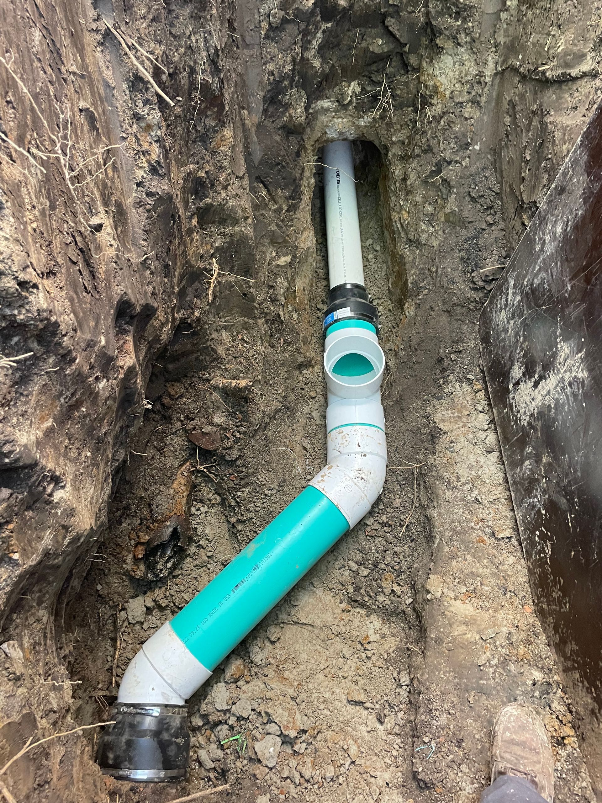 PVC pipes in a trench, a teal pipe with white and black connections.