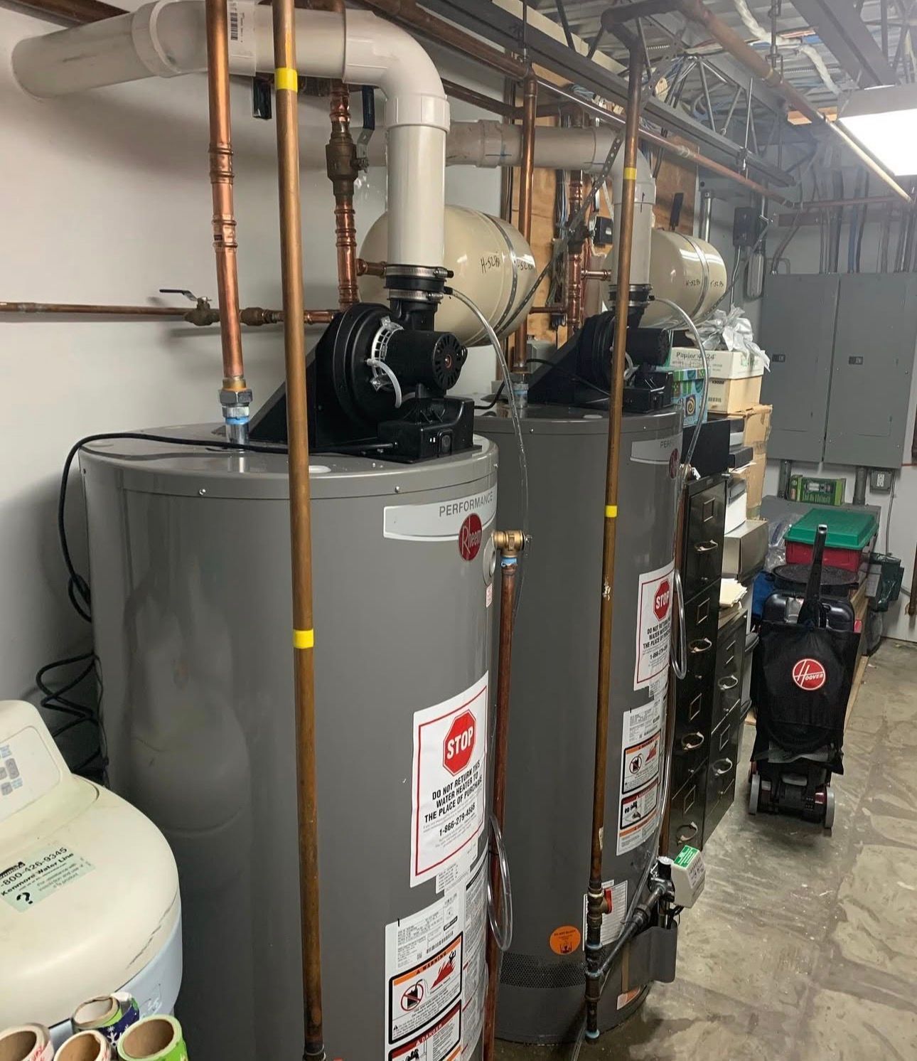 Two gray water heaters with copper pipes in an industrial setting.