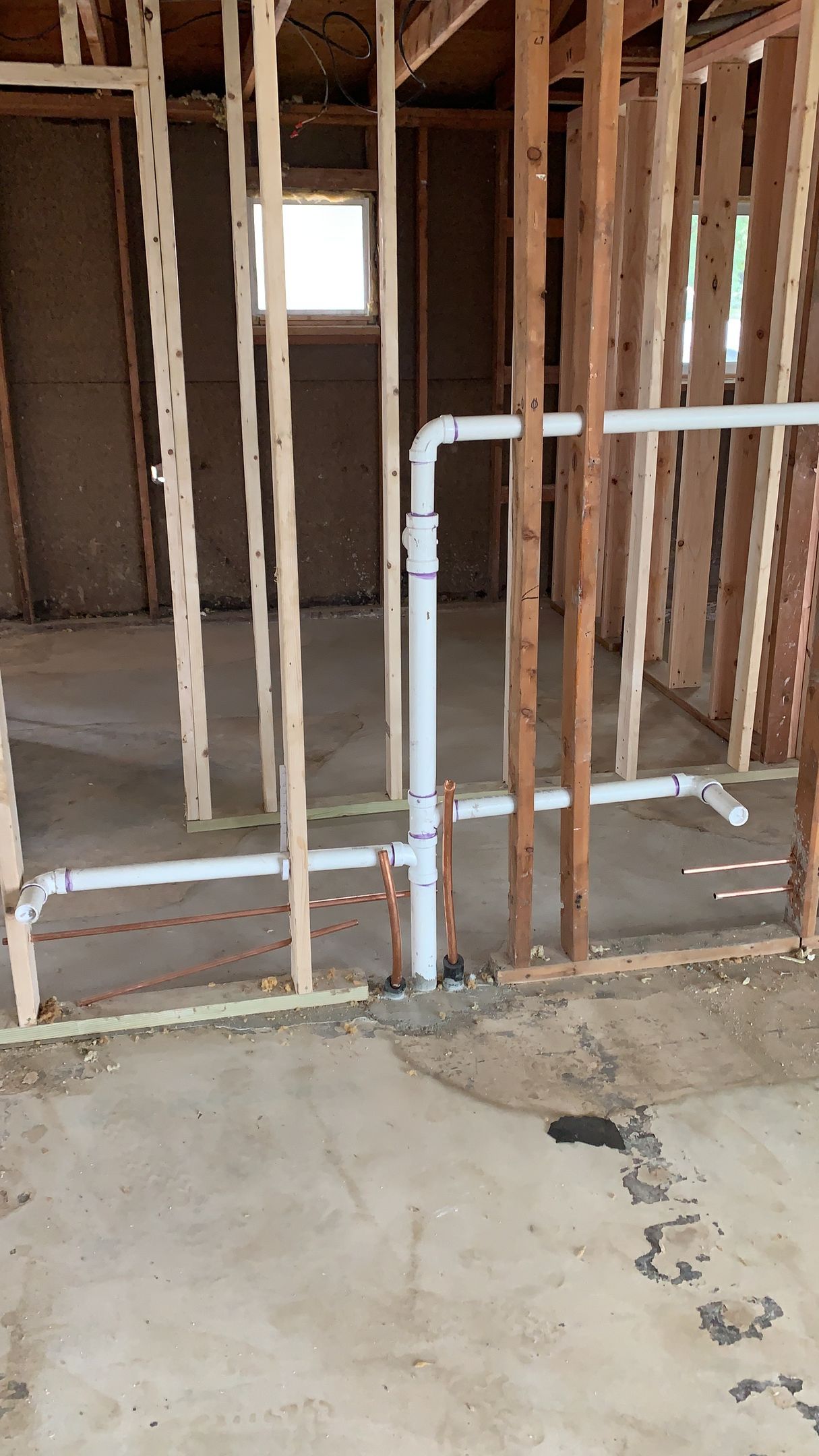 Interior view of a partially framed wall with white PVC pipes for plumbing visible. Concrete floor.
