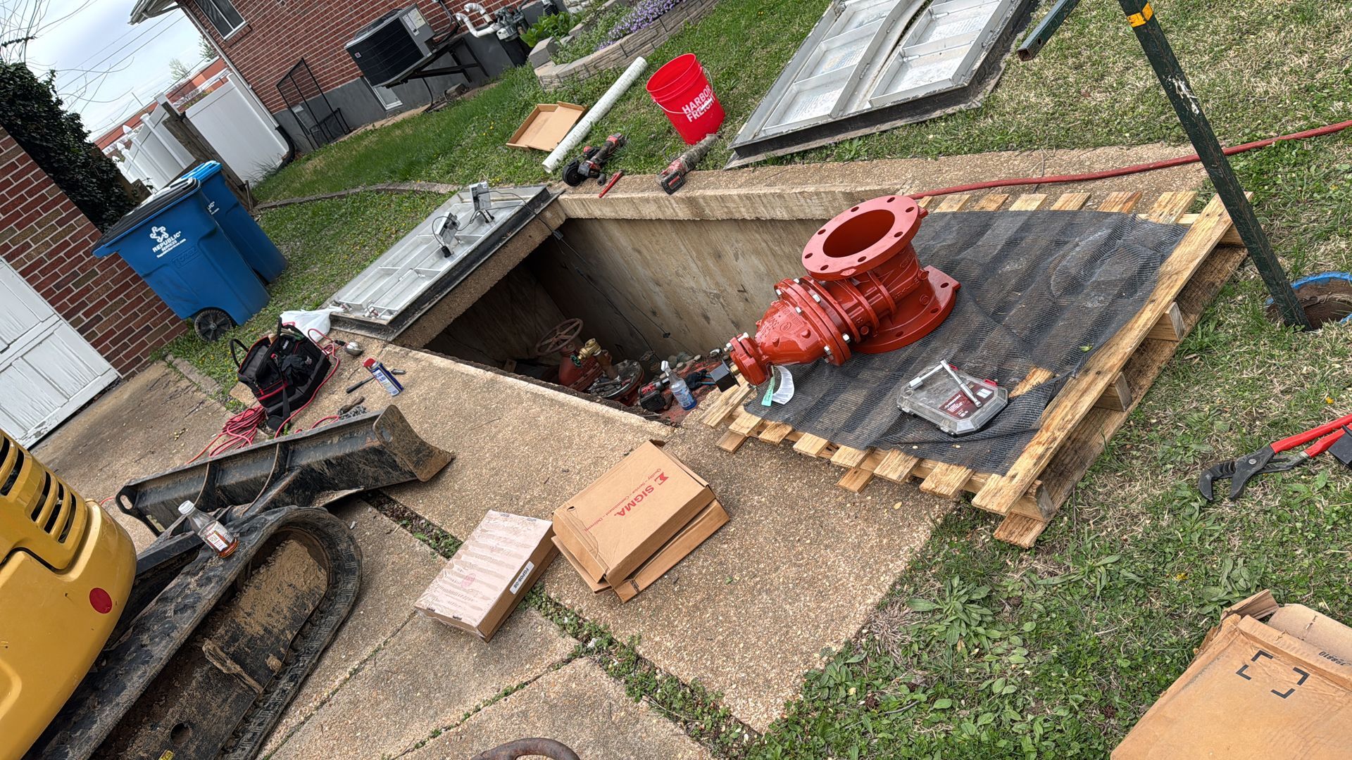 Open underground utility vault, open, red pump, tools, and construction materials on a pallet.