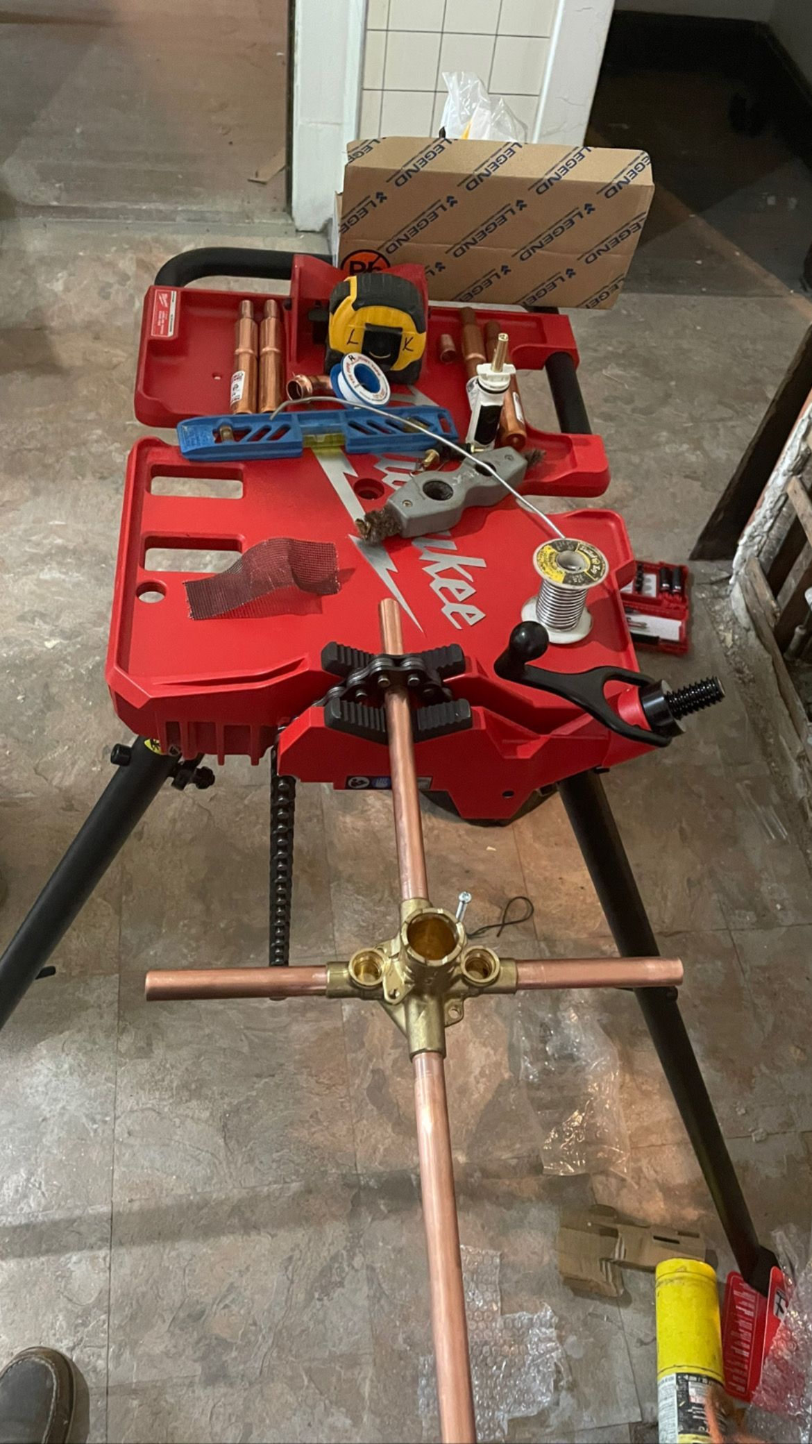 Plumbing tools laid out on a red toolbox stand; copper pipes and fittings ready for assembly.