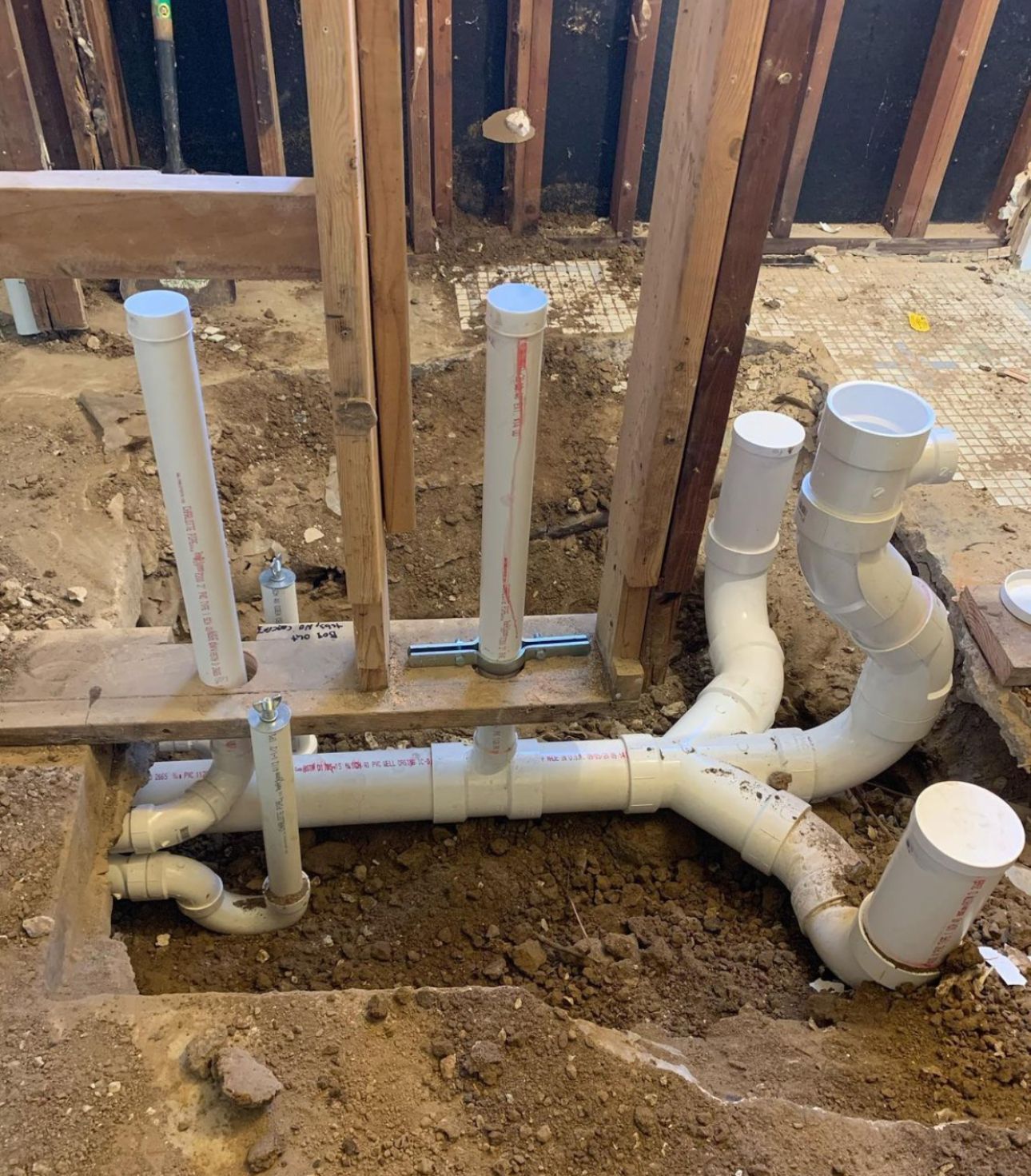 Plumbing pipes in a bathroom renovation, showing drain and vent lines. White PVC pipes are connected to wooden studs.