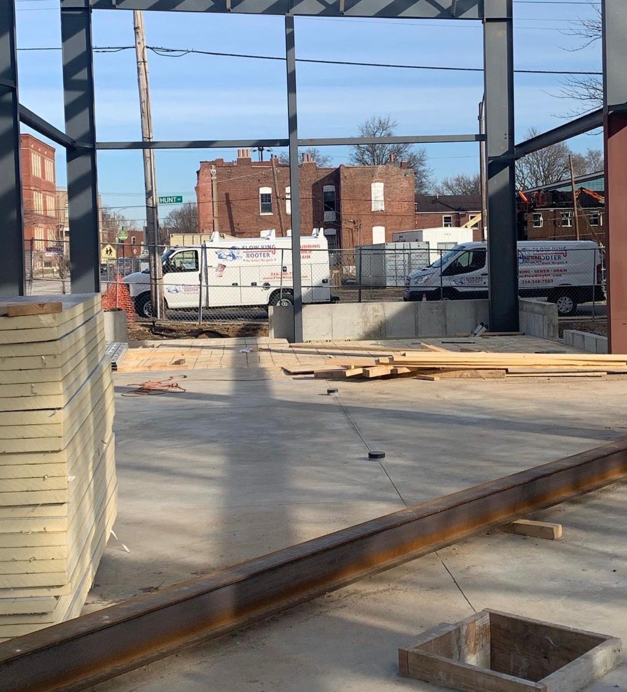 Construction site: Steel frame, concrete floor, view of street with parked vans and brick buildings.