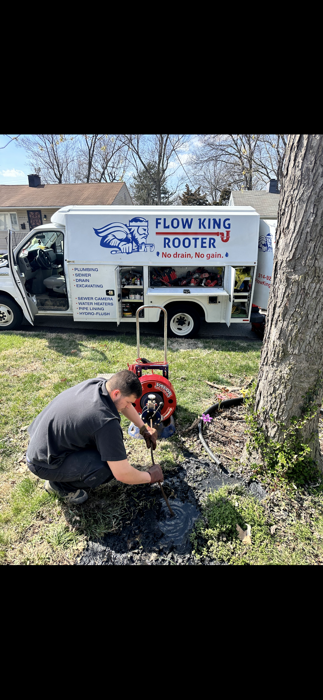 Man using power tools near a tree with a company truck in the background.