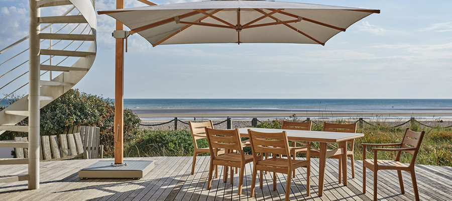 A wooden deck with a table and chairs under an umbrella overlooking the ocean.