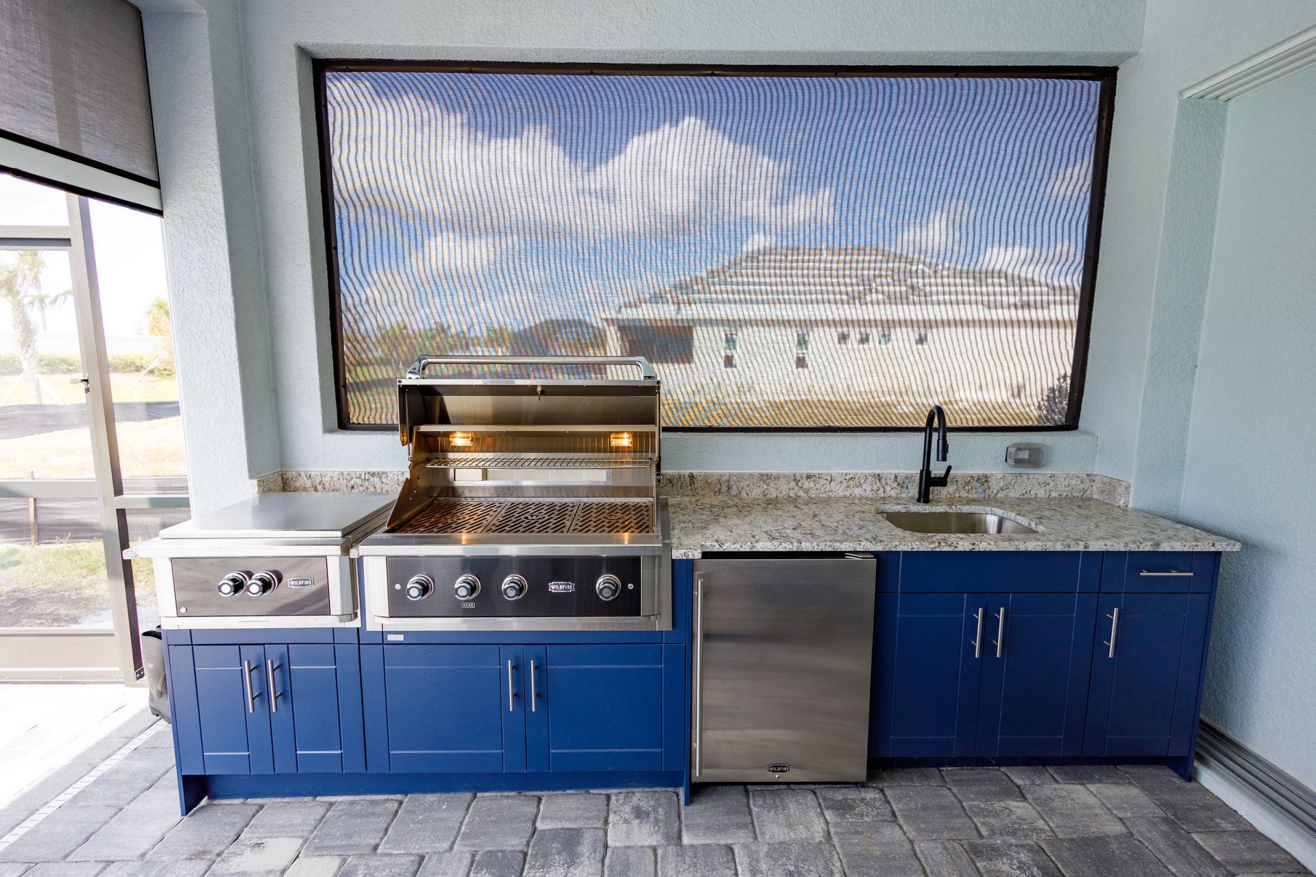 A kitchen with blue cabinets, a grill, a sink and a window
