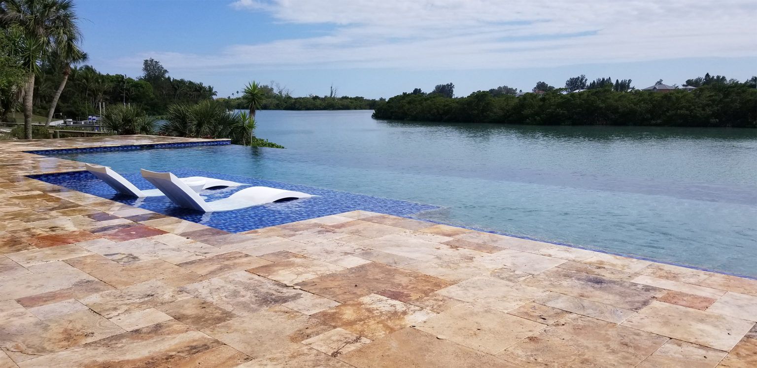 A large swimming pool surrounded by a stone wall next to a body of water.