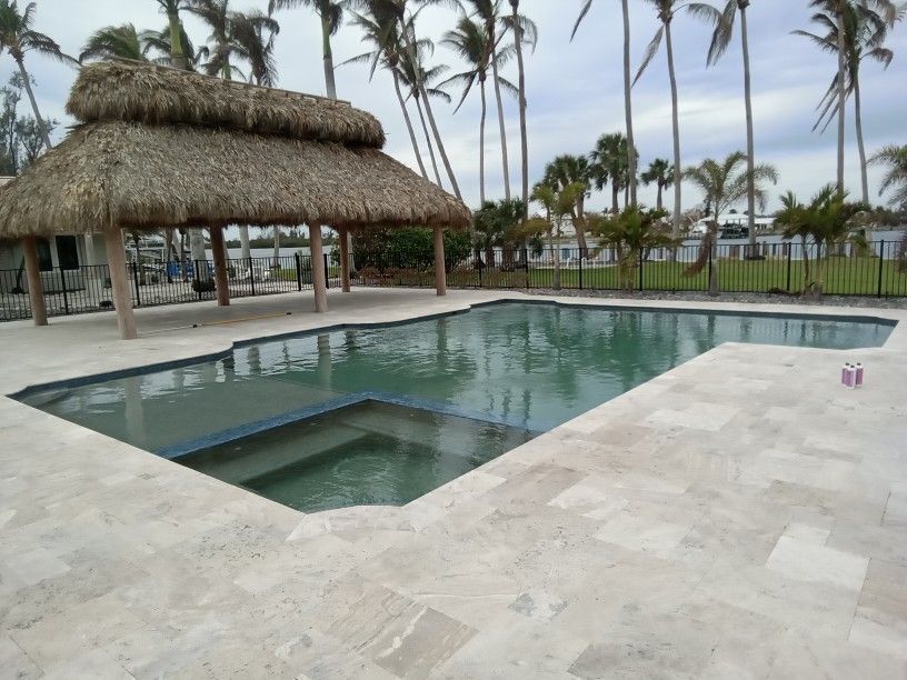 A swimming pool with a thatched roof and palm trees in the background.