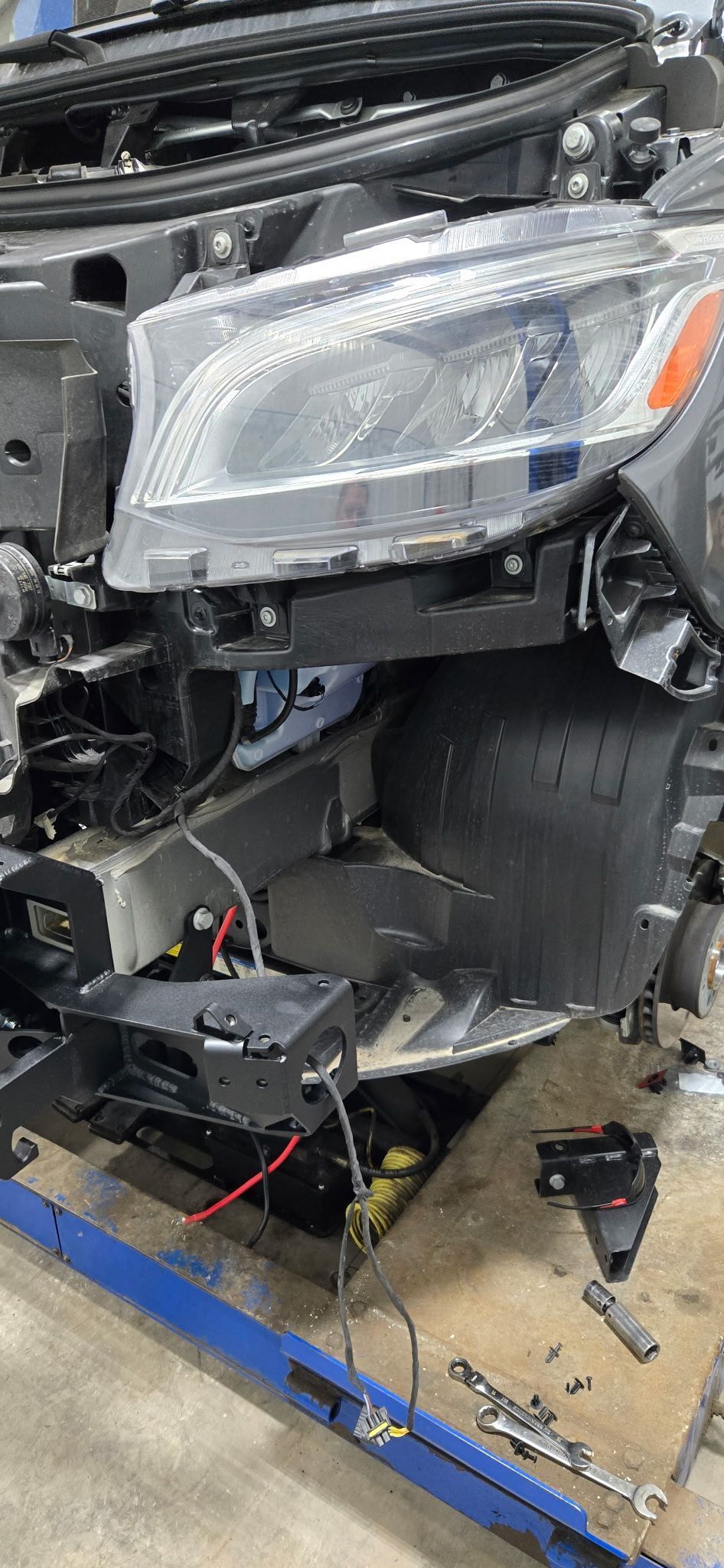 Damaged car front end, headlight, exposed components, repair work in progress.