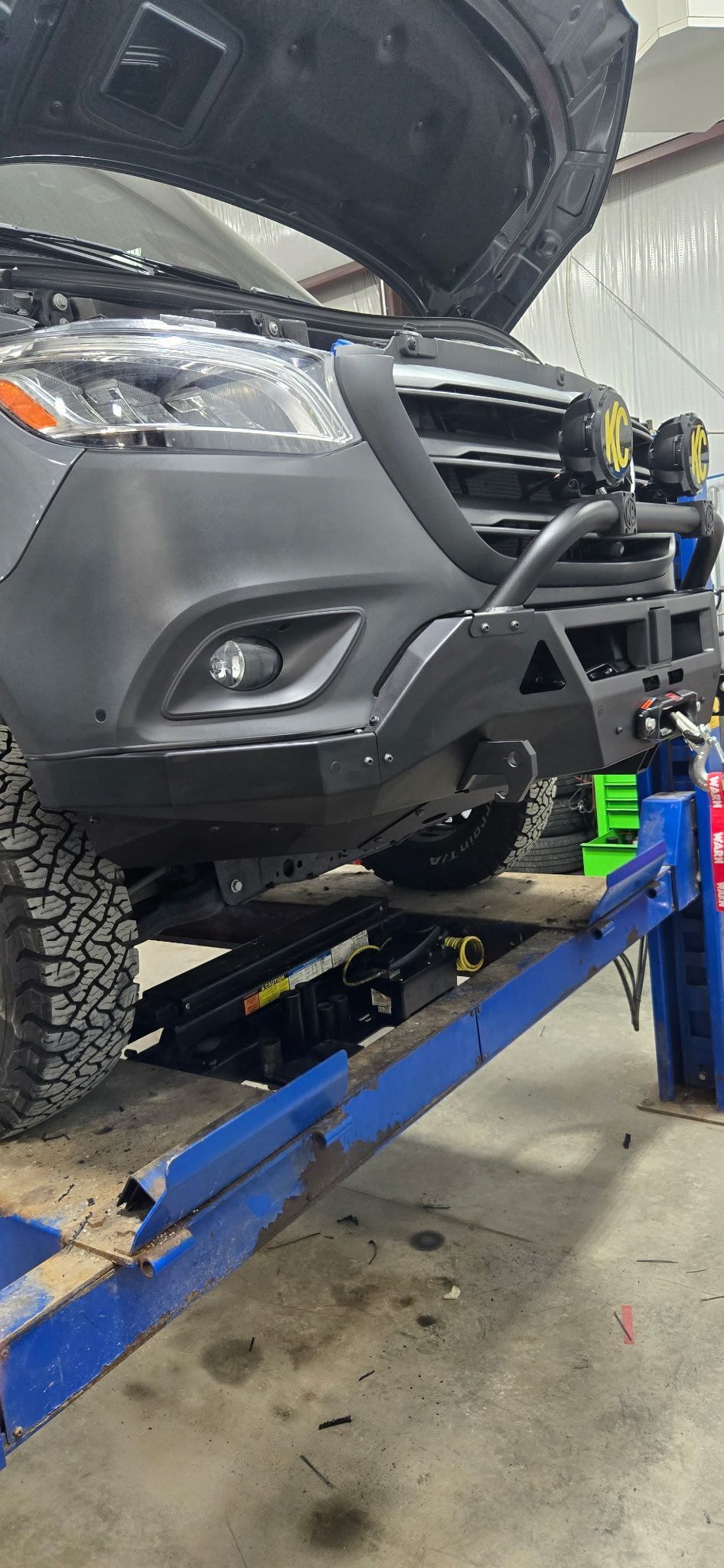 A black van with open hood is on a blue lift in a garage.