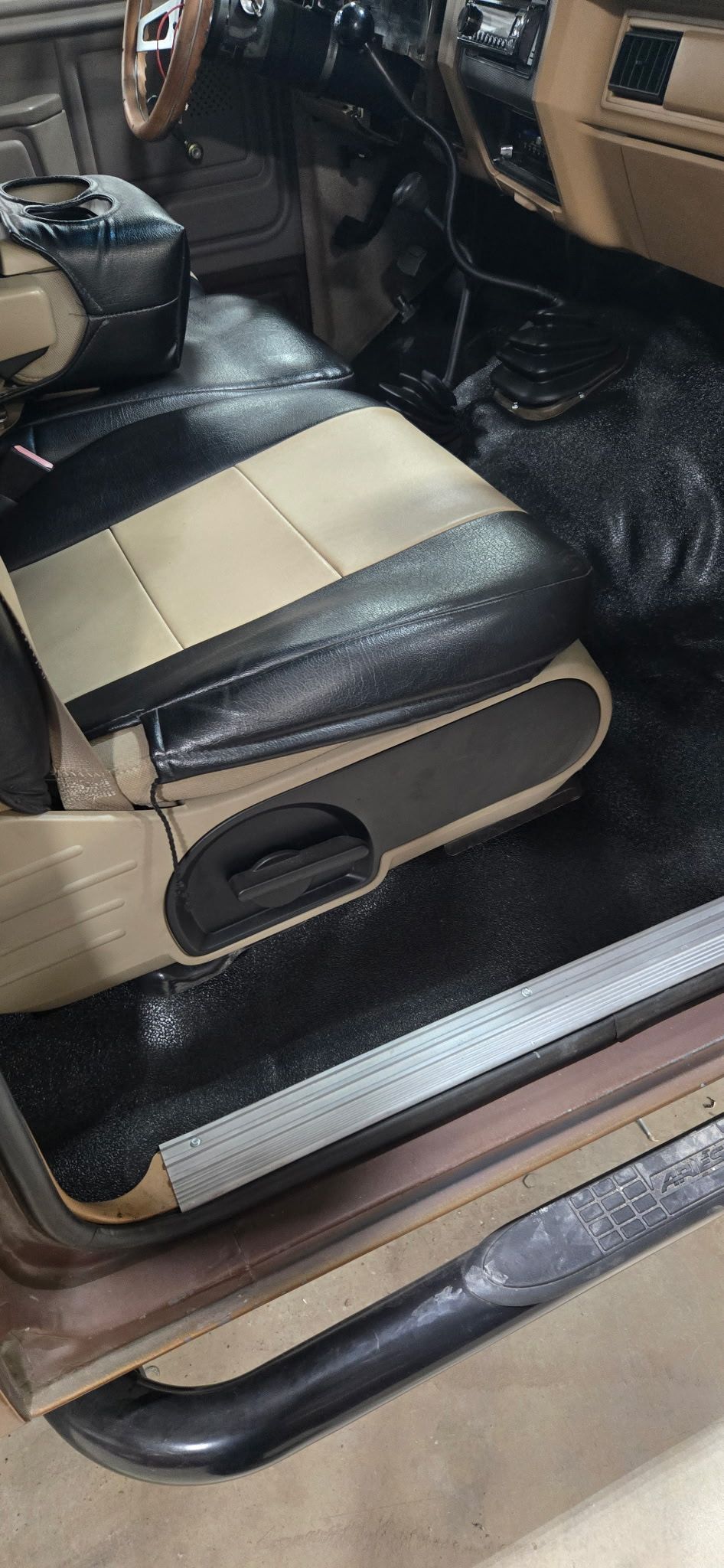 Interior of a vehicle with a black and beige seat, a black step rail, and a black floor.