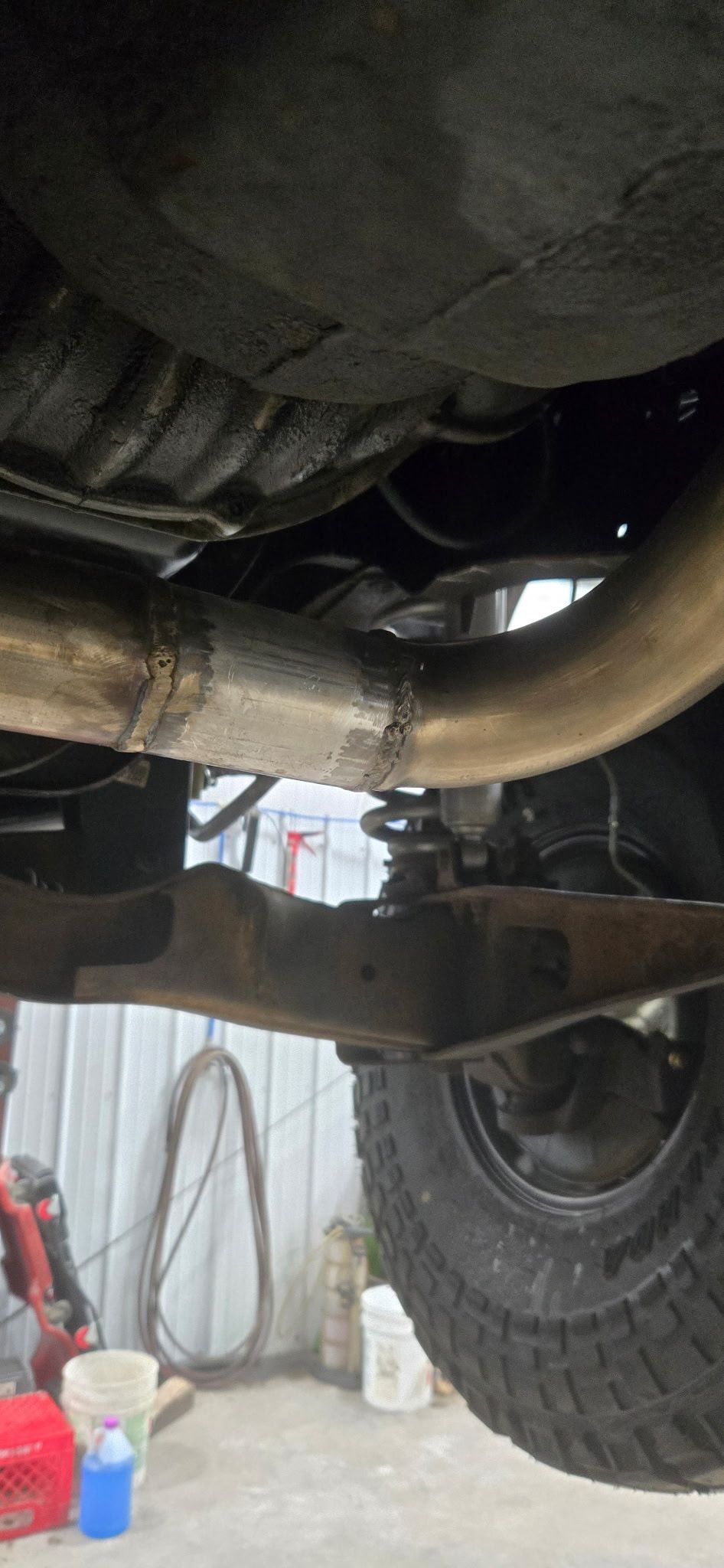 Underside of a vehicle showing an exhaust pipe, suspension components, and tire.