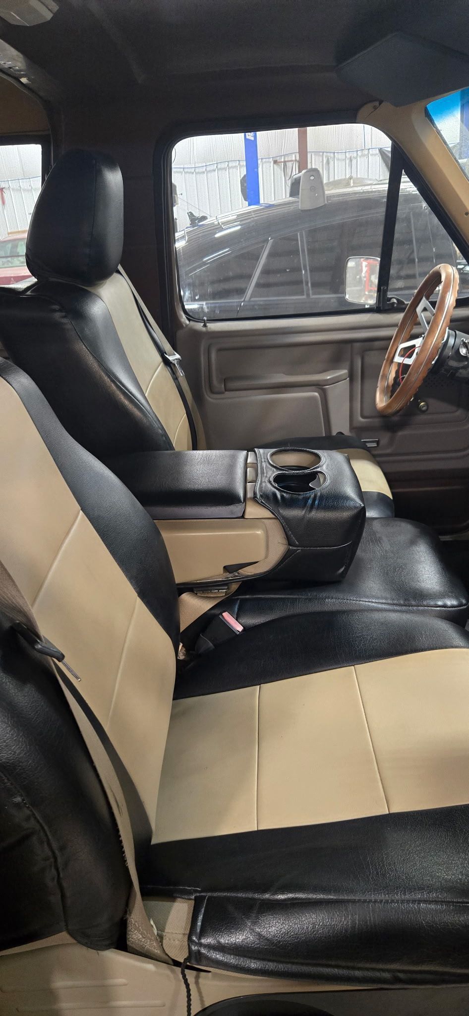 Interior of a classic truck. Black and tan seats, wooden steering wheel, center console visible.