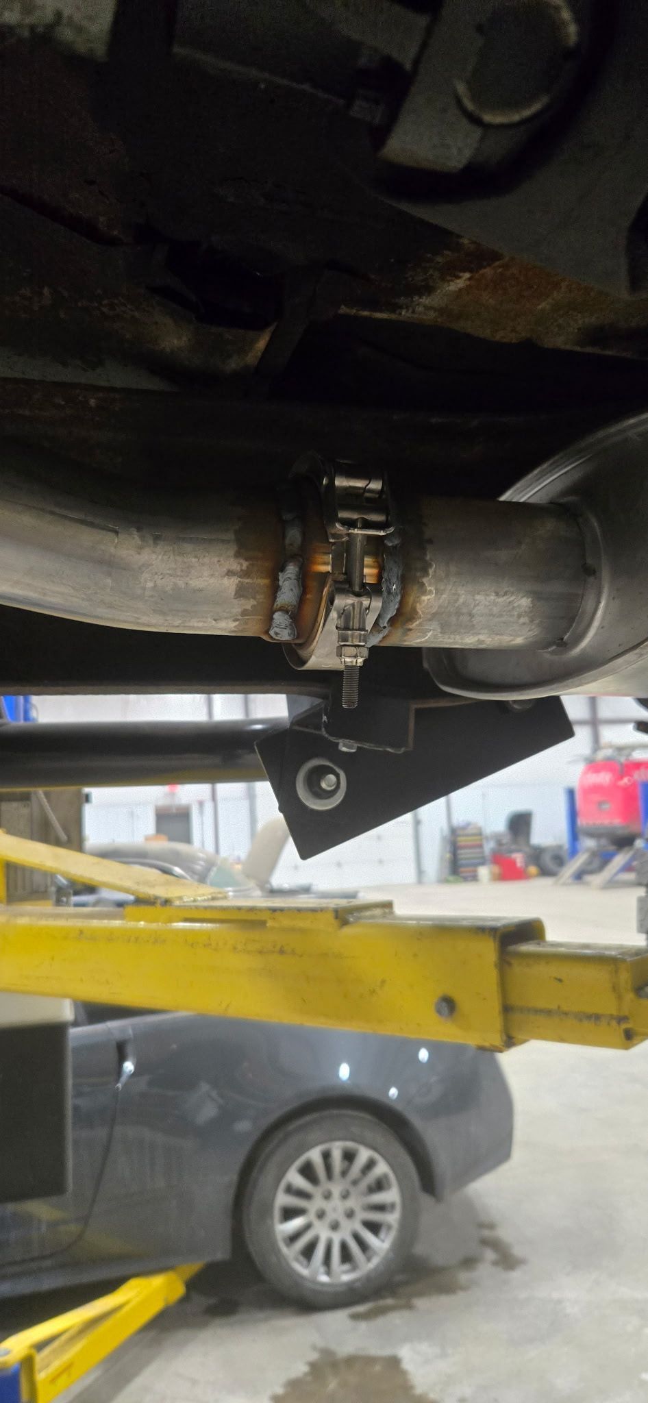 Exhaust pipe with clamp and a support bracket attached to a vehicle lifted on a yellow lift.