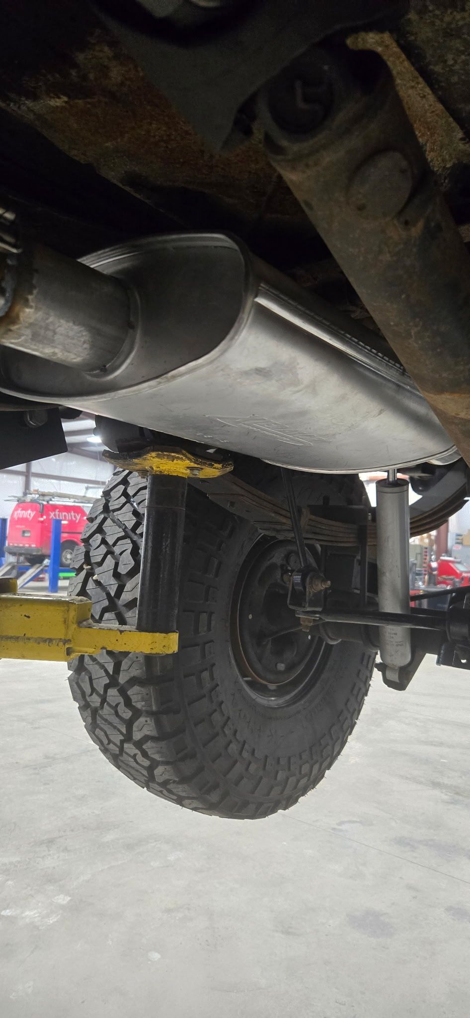 Underside of a vehicle showing the exhaust system, tires, and suspension on a lift.