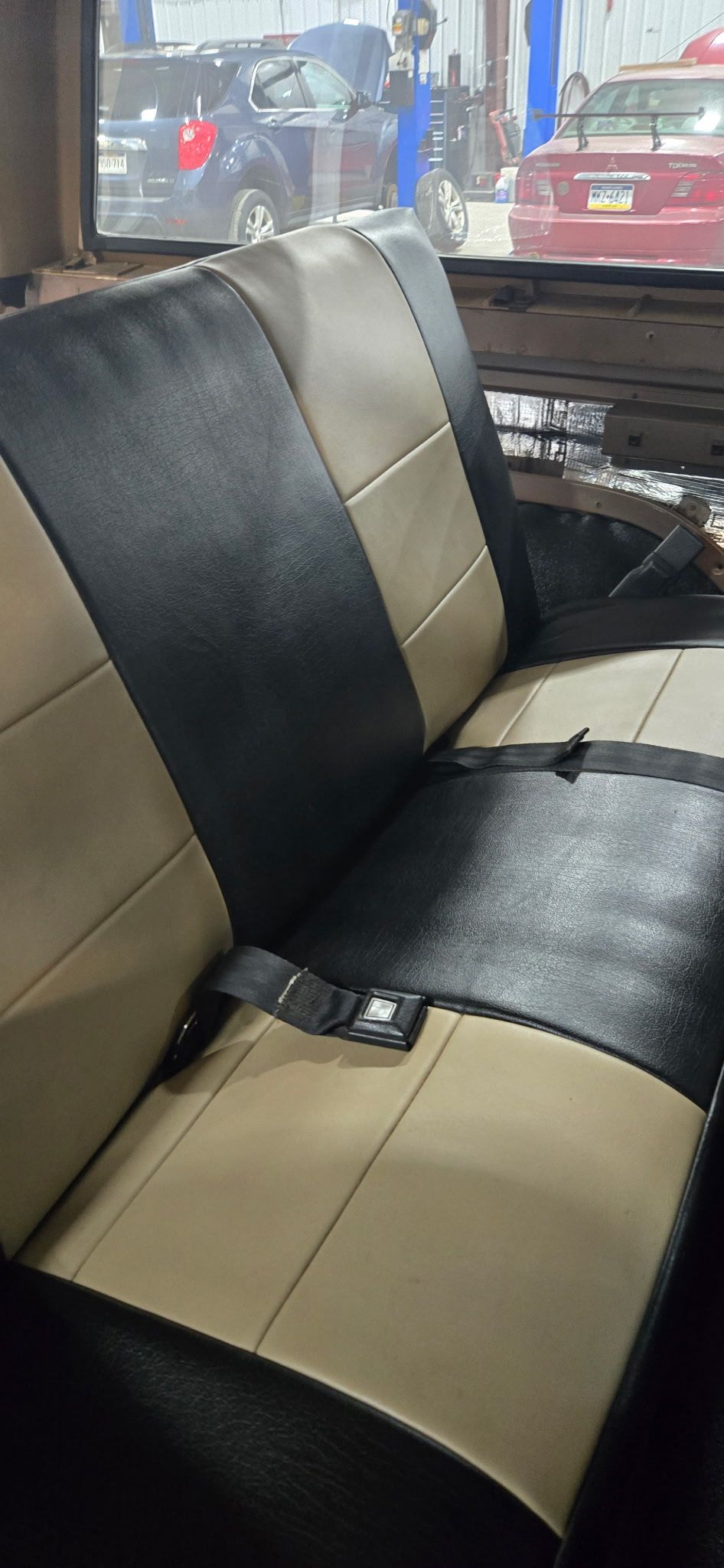 Interior car seat with black and tan upholstery and a seat belt, viewed from an angle.