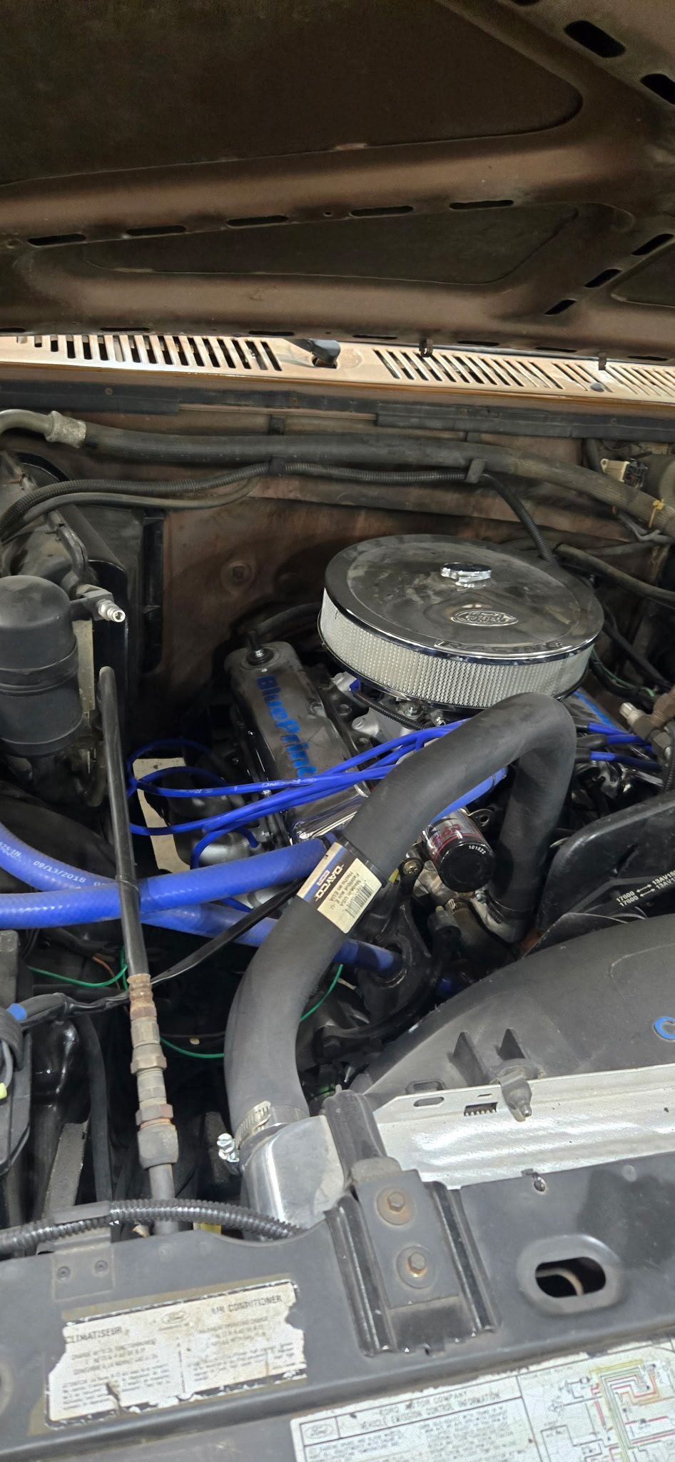 Engine bay of a dark-colored car with blue hoses and a chrome air filter.