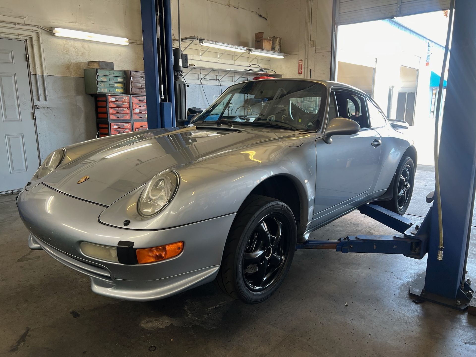 Silver Porsche sports car on a lift in a repair shop.