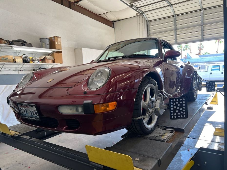 A red Porsche convertible on a car lift in a repair shop for wheel alignment.