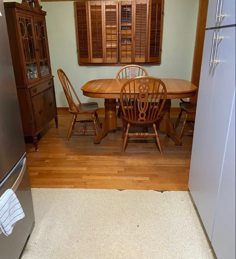 Small dining area with wooden table, chairs, and cabinet on a wooden floor - Before