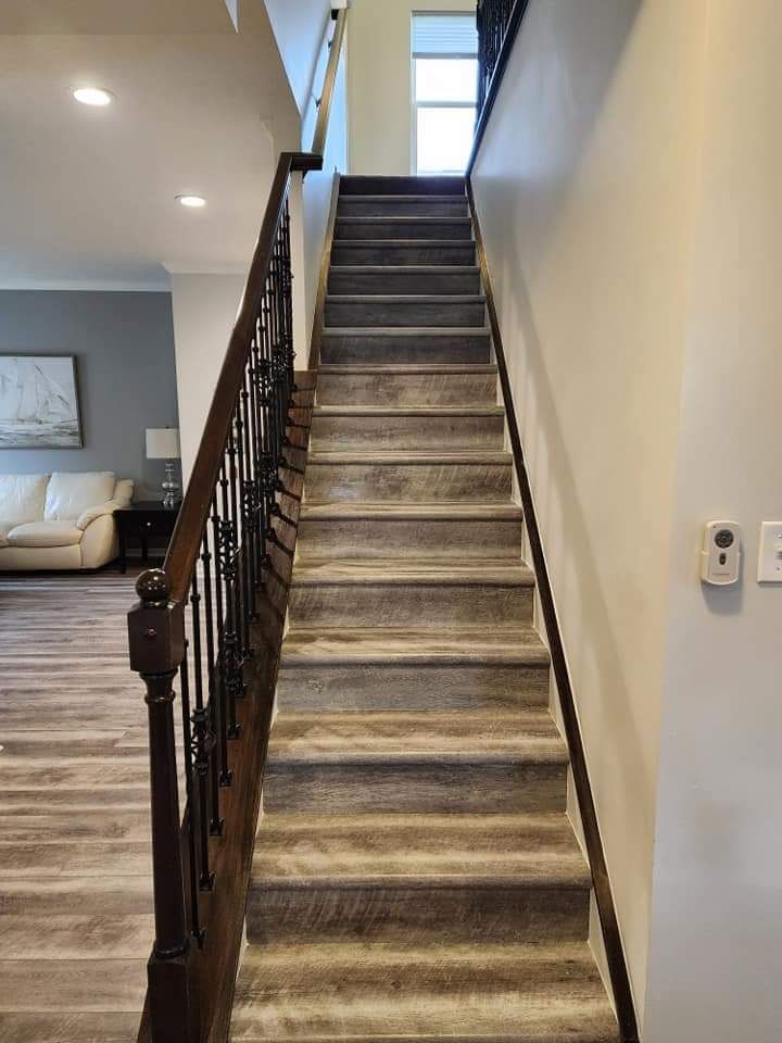 Narrow carpeted staircase in a beige hallway with dark wood railing and a window at the top.