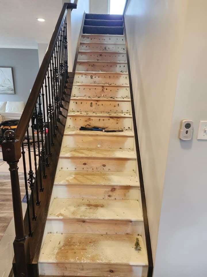 Narrow carpeted staircase with black railing, leading up between white walls