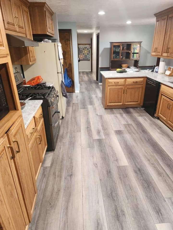 Kitchen with wooden cabinets, gray wood-look flooring, gas stove, and island with sink.