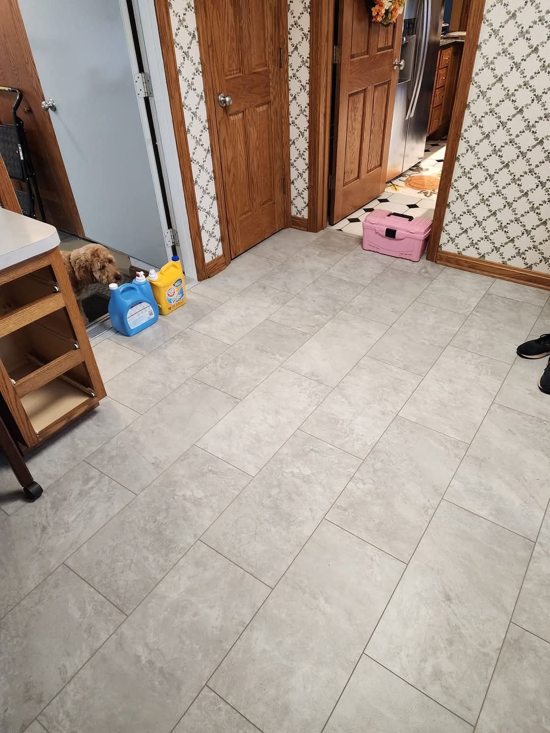 Tiled room floor with wooden doors, a pink stool, and household items near the wall.