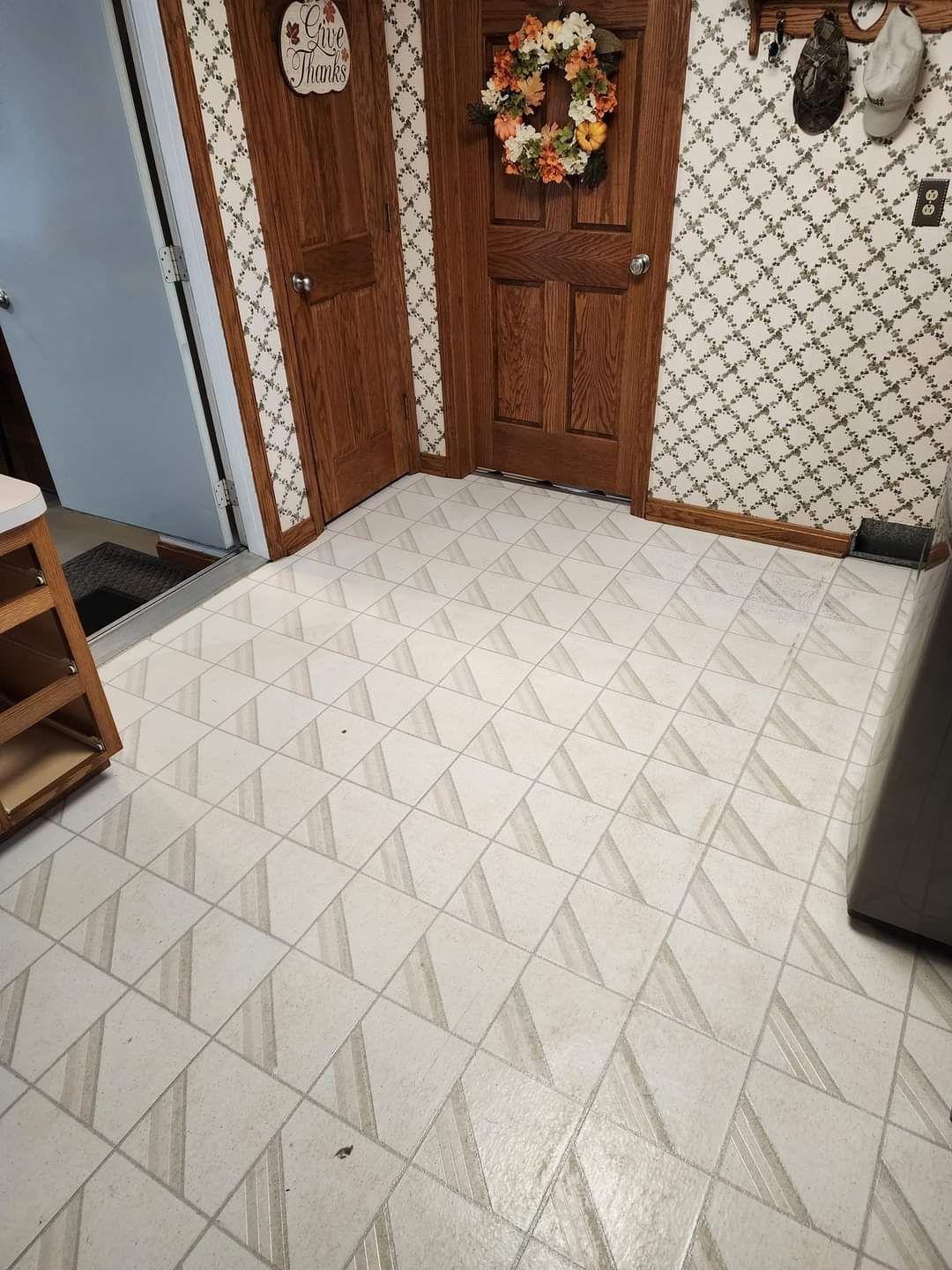 Indoor tiled entryway with wooden front doors, a floral wreath, and a small shelf on the left.