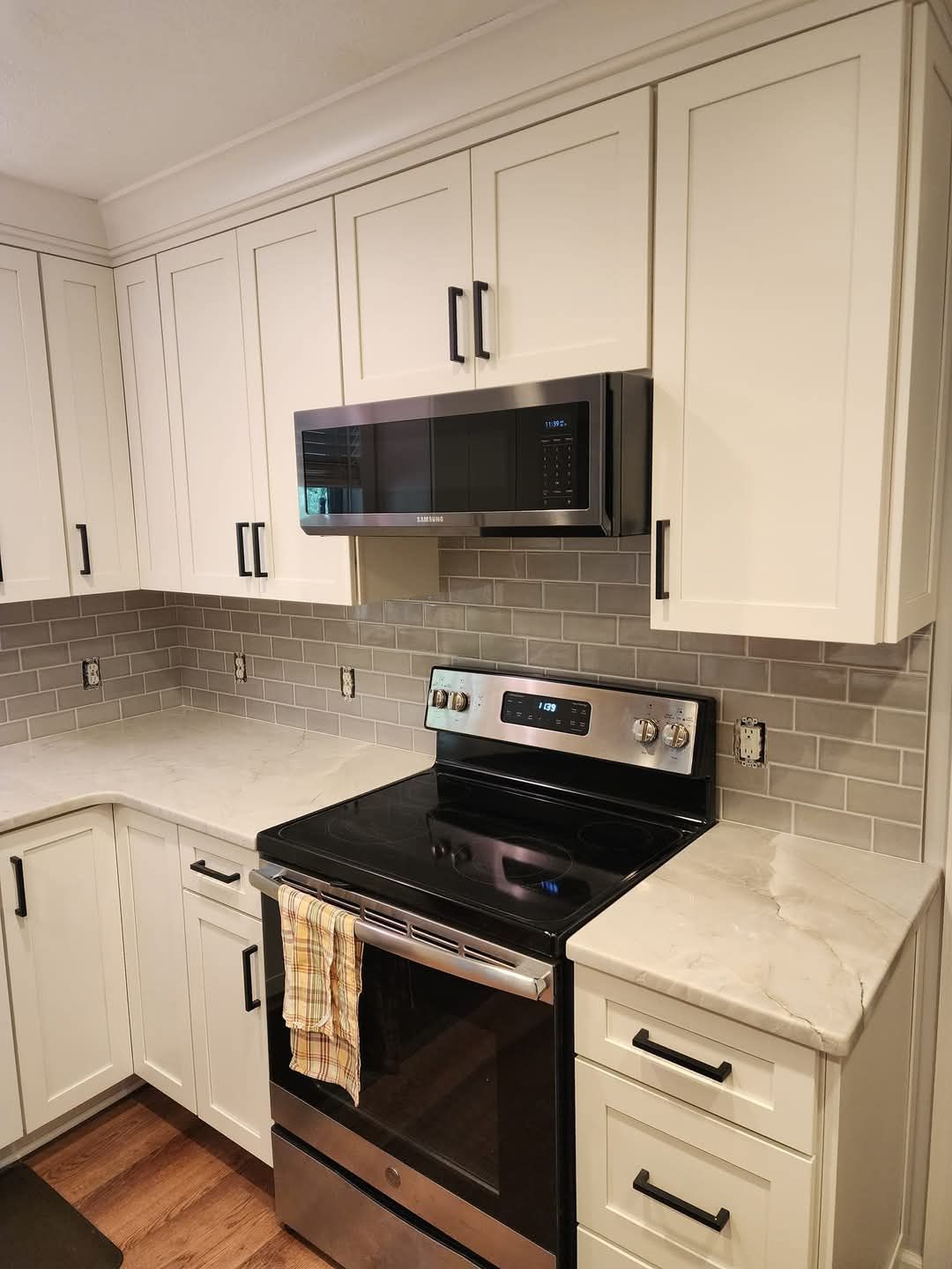 Modern white kitchen with black stove and microwave, gray tile backsplash, and light countertops