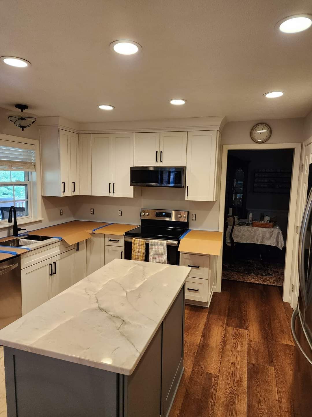 Bright modern kitchen with white cabinets, marble island, wood floors, and recessed ceiling lights