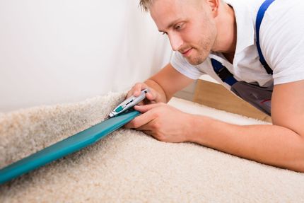 Person using a handheld vacuum to clean carpet along the baseboard
