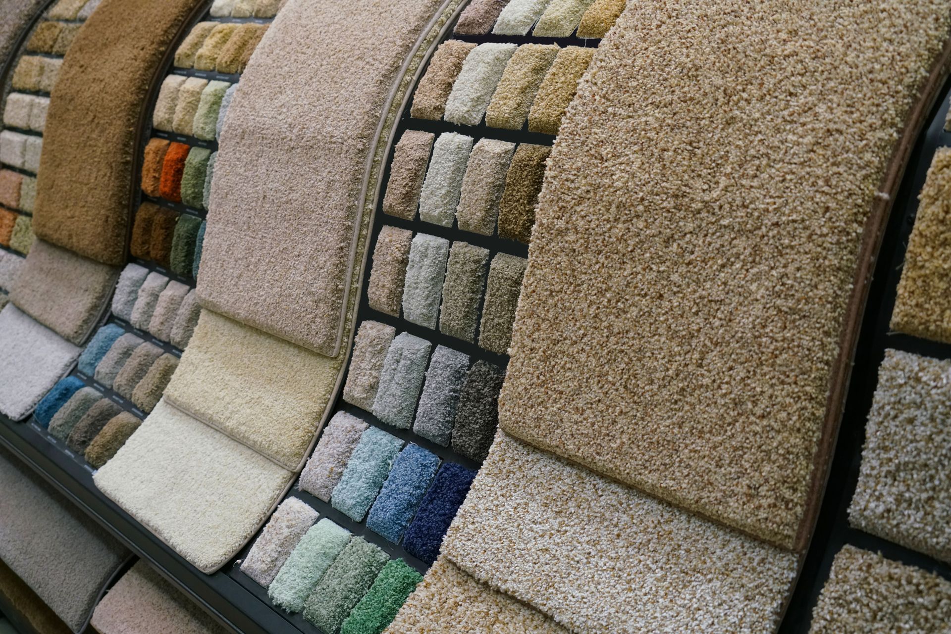 Rows of colorful carpet samples displayed in a showroom, including beige, blue, and green textures