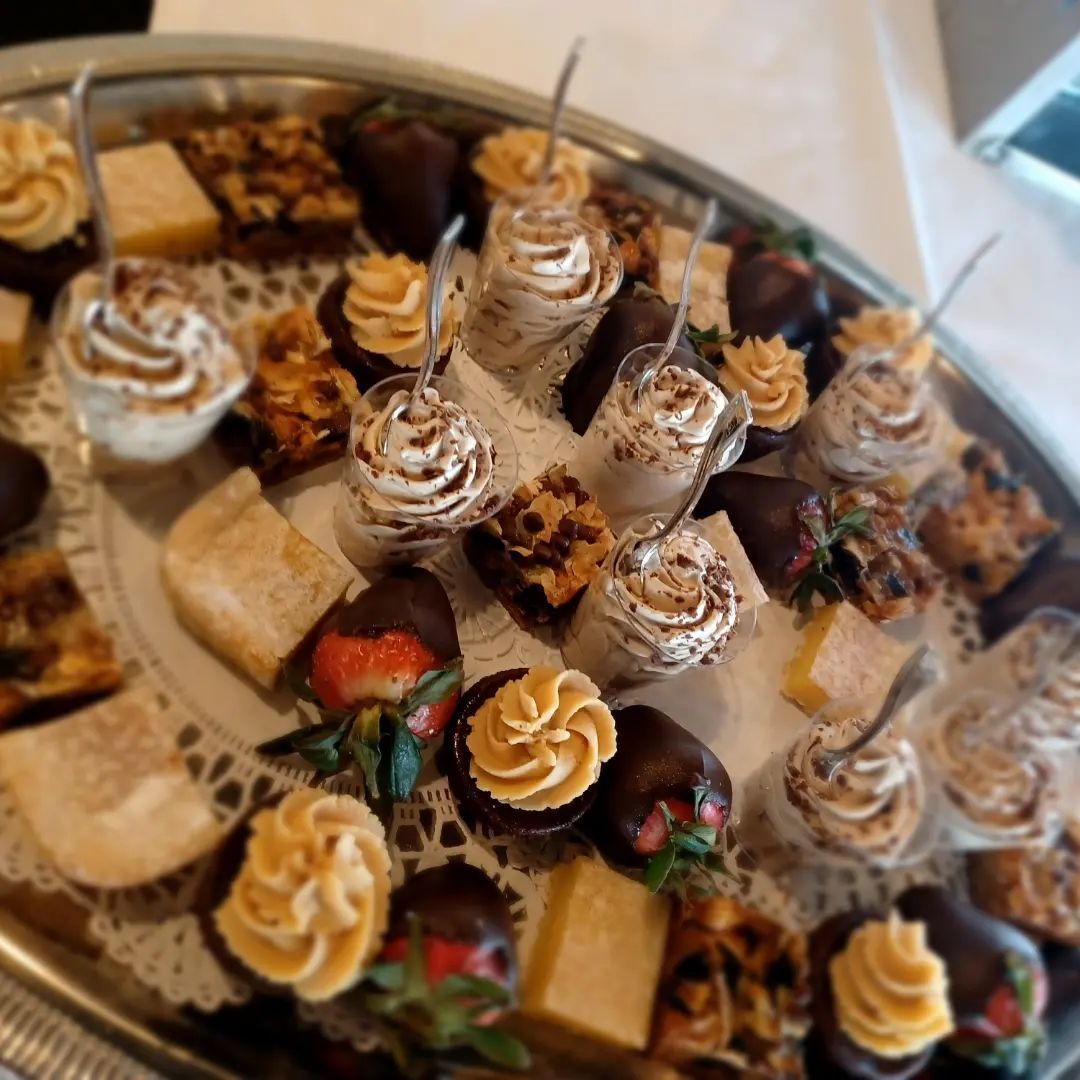 A silver platter holds an assortment of small desserts, including chocolate-covered strawberries, pastries, and parfaits.