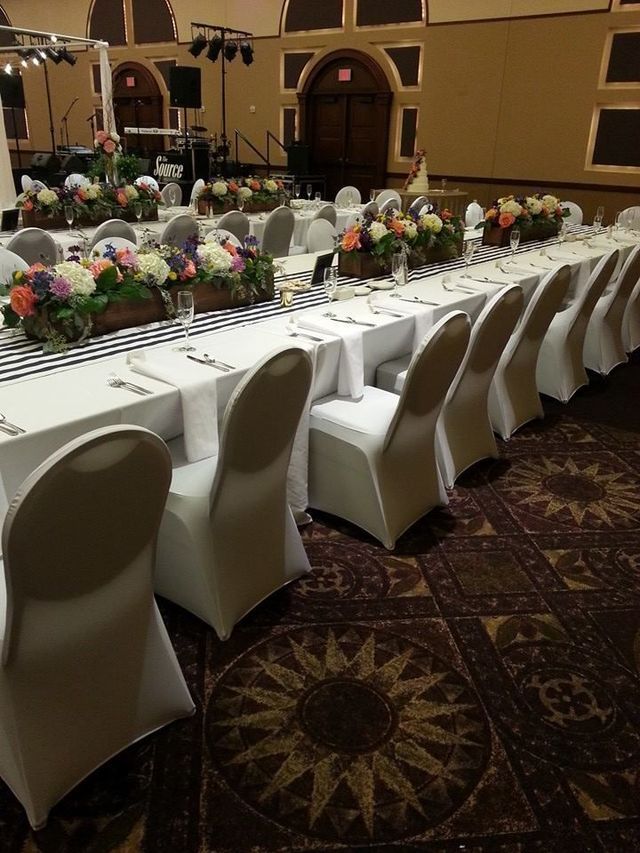 Long banquet tables set with white linens, black striped runners, and floral centerpieces in a formal event hall.