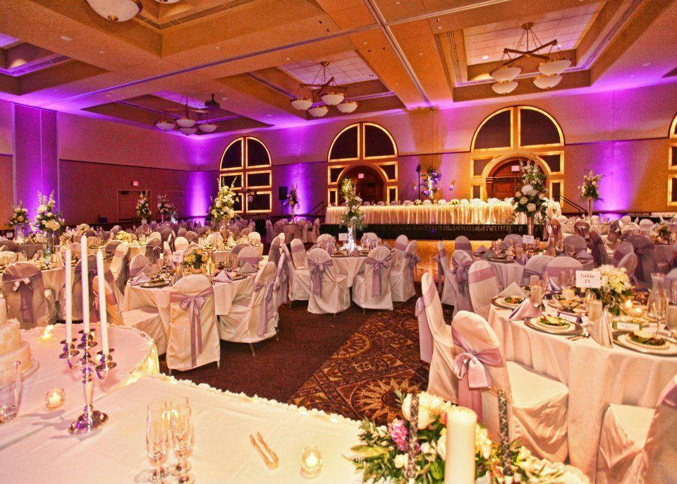 A banquet hall set for a wedding reception with round tables, white tablecloths, purple lighting, and floral centerpieces.