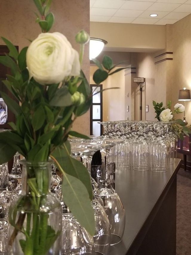 A white flower in a glass vase sits on a counter next to several empty upside-down wine glasses in a dimly lit room.