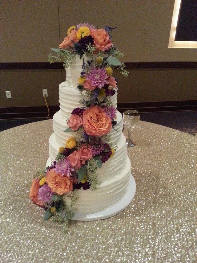 A five-tier, white-frosted wedding cake decorated with a cascading arrangement of orange, purple, and yellow flowers.