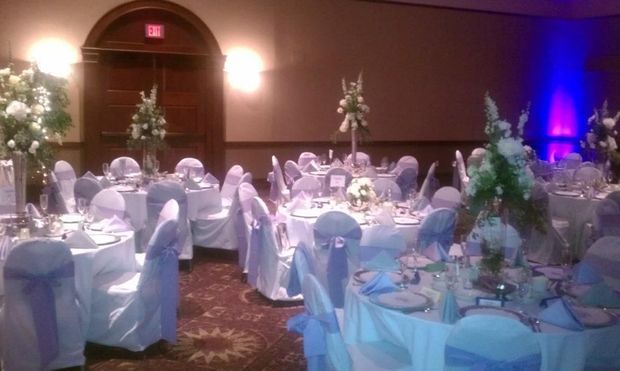 A ballroom setup for a formal event with round tables featuring white linens, blue sashes, and floral centerpieces.