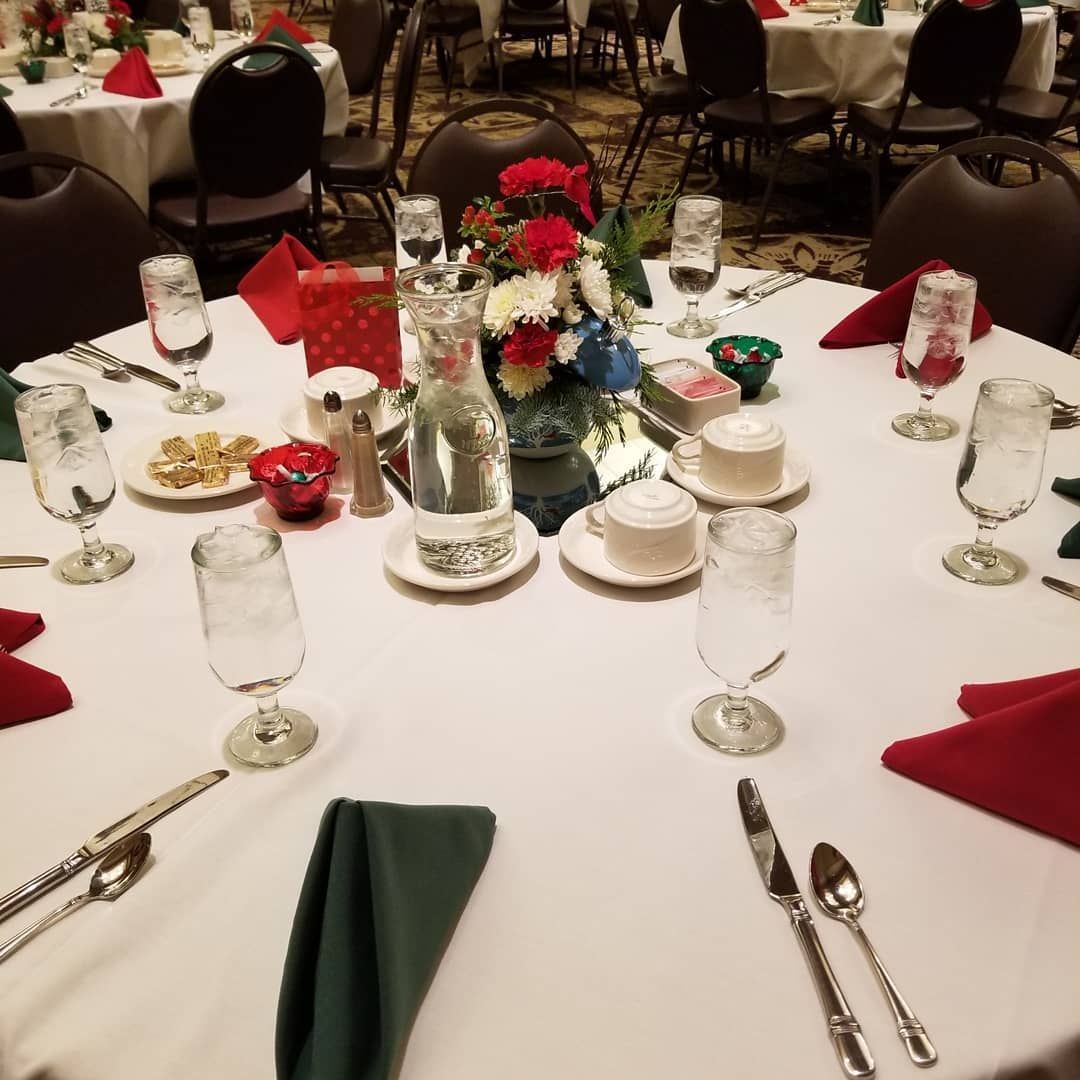 A round banquet table set for dinner with a floral centerpiece, glassware, silverware, and red and green napkins.