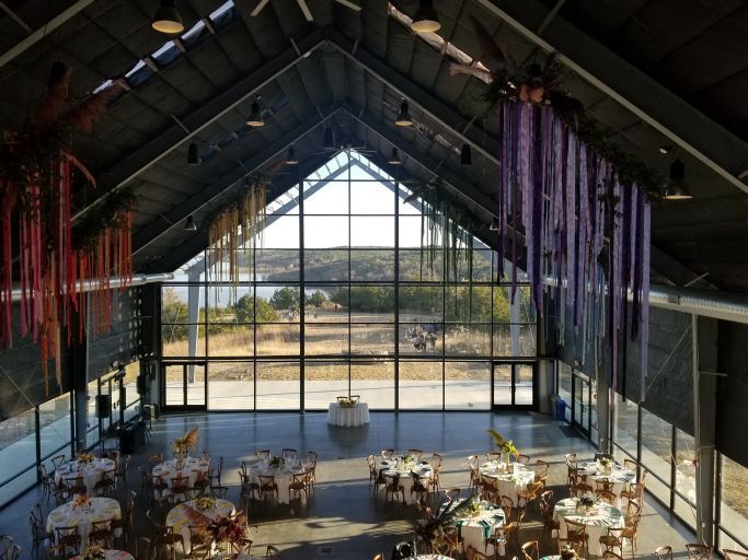 High-angle view of a modern wedding hall with floor-to-ceiling windows overlooking a landscape and decorative streamers.