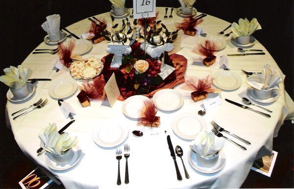 A round dining table is set for a formal event with place settings, floral centerpieces, and a numbered table sign.