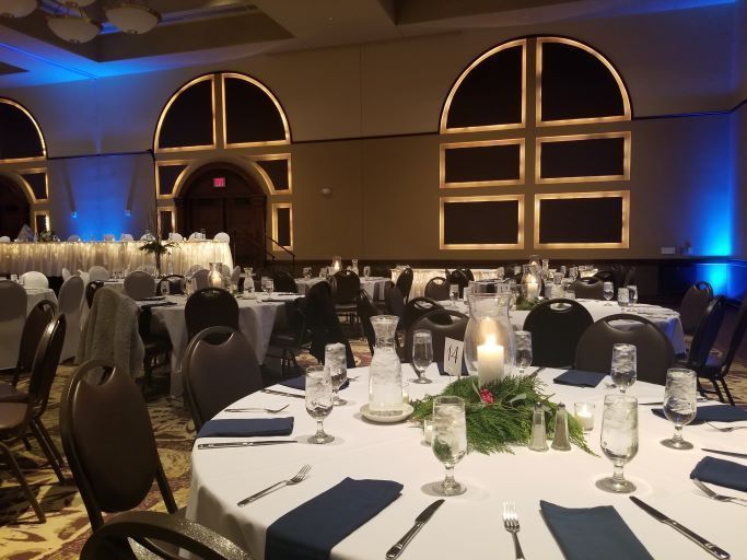 A banquet hall prepared for an event with round tables featuring white tablecloths, navy napkins, and candle centerpieces.