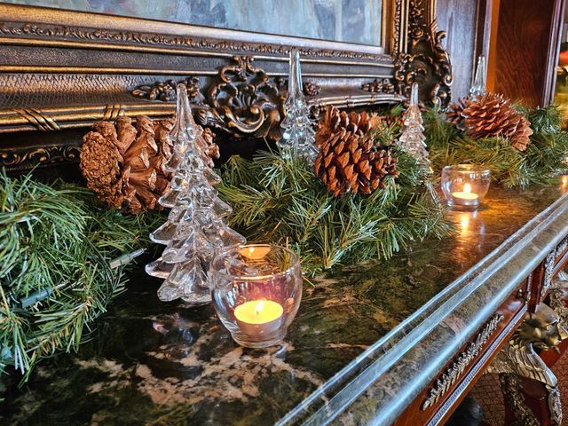 A mantle decorated with greenery, pinecones, clear glass trees, and glowing tealight candles in glass holders.