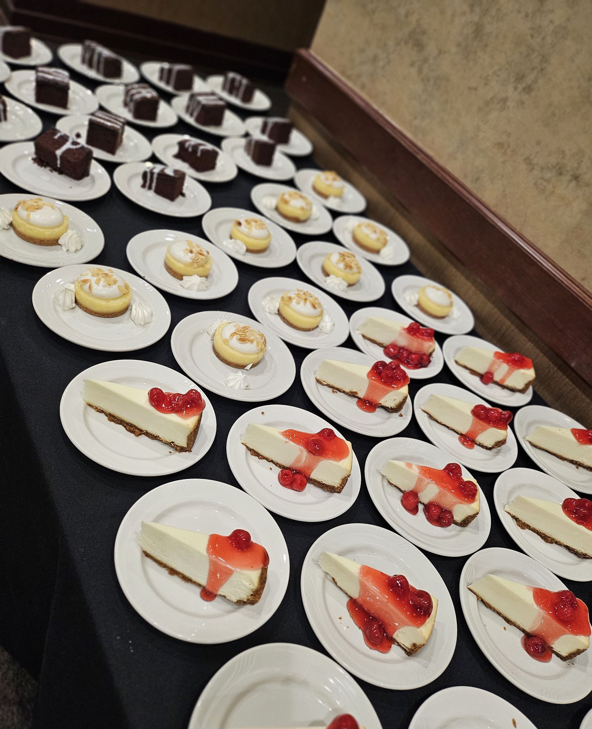 Plates of cheesecake slices with strawberry topping and smaller dessert cakes arranged on a table.
